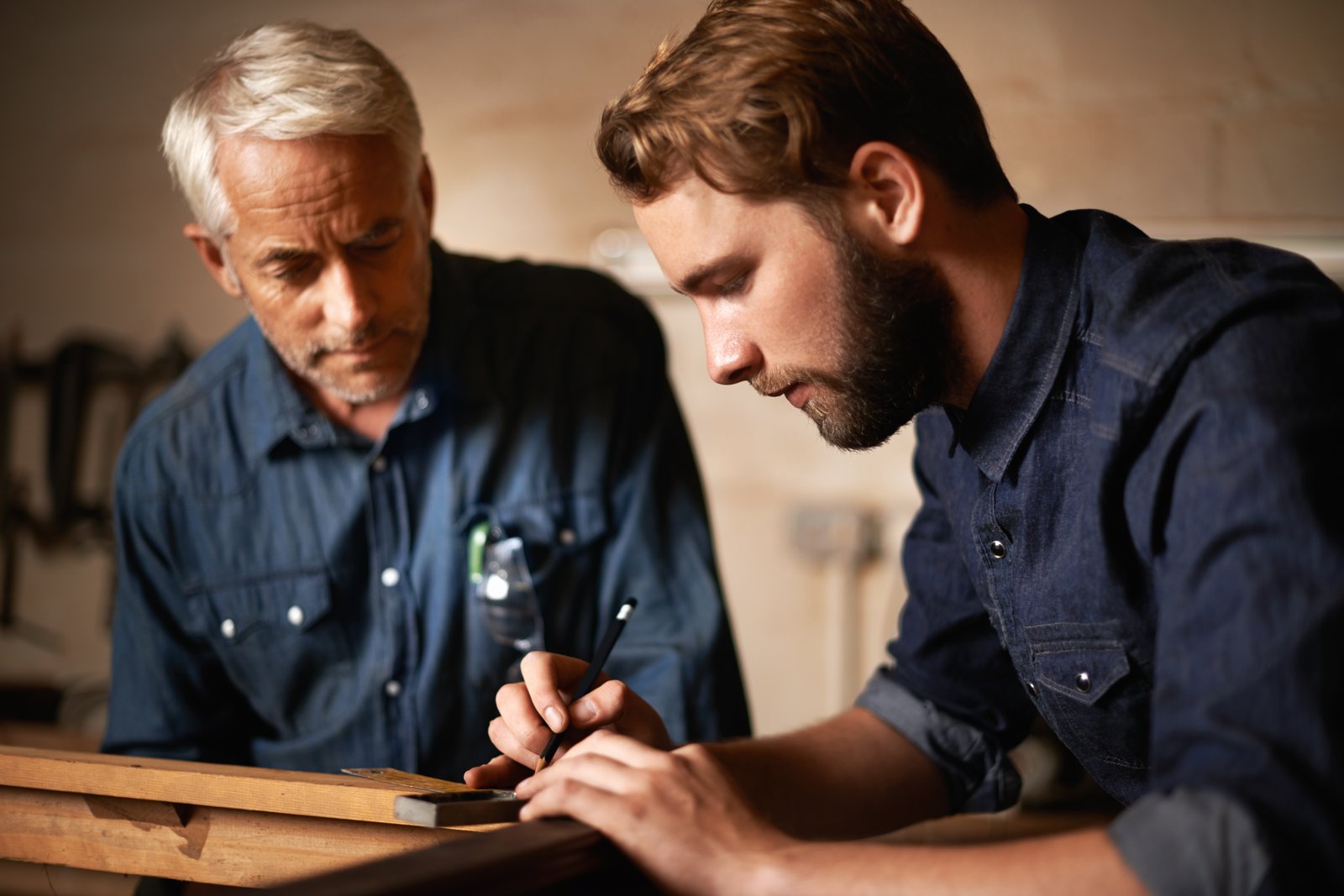 A mentor and apprentice measuring wood together in a formal training workshop A mentor and apprentice measuring wood together in a formal training workshop