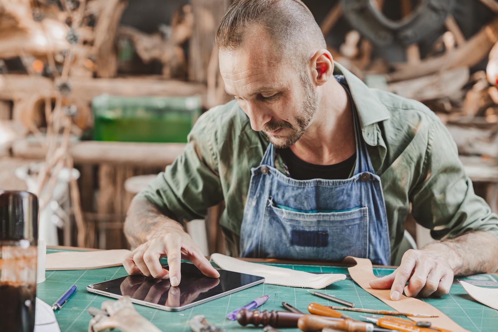 A leather craftsman using a digital tablet at his workbench, where craftsmanship meets Industry 5.0 A leather craftsman using a digital tablet at his workbench, where craftsmanship meets Industry 5.0
