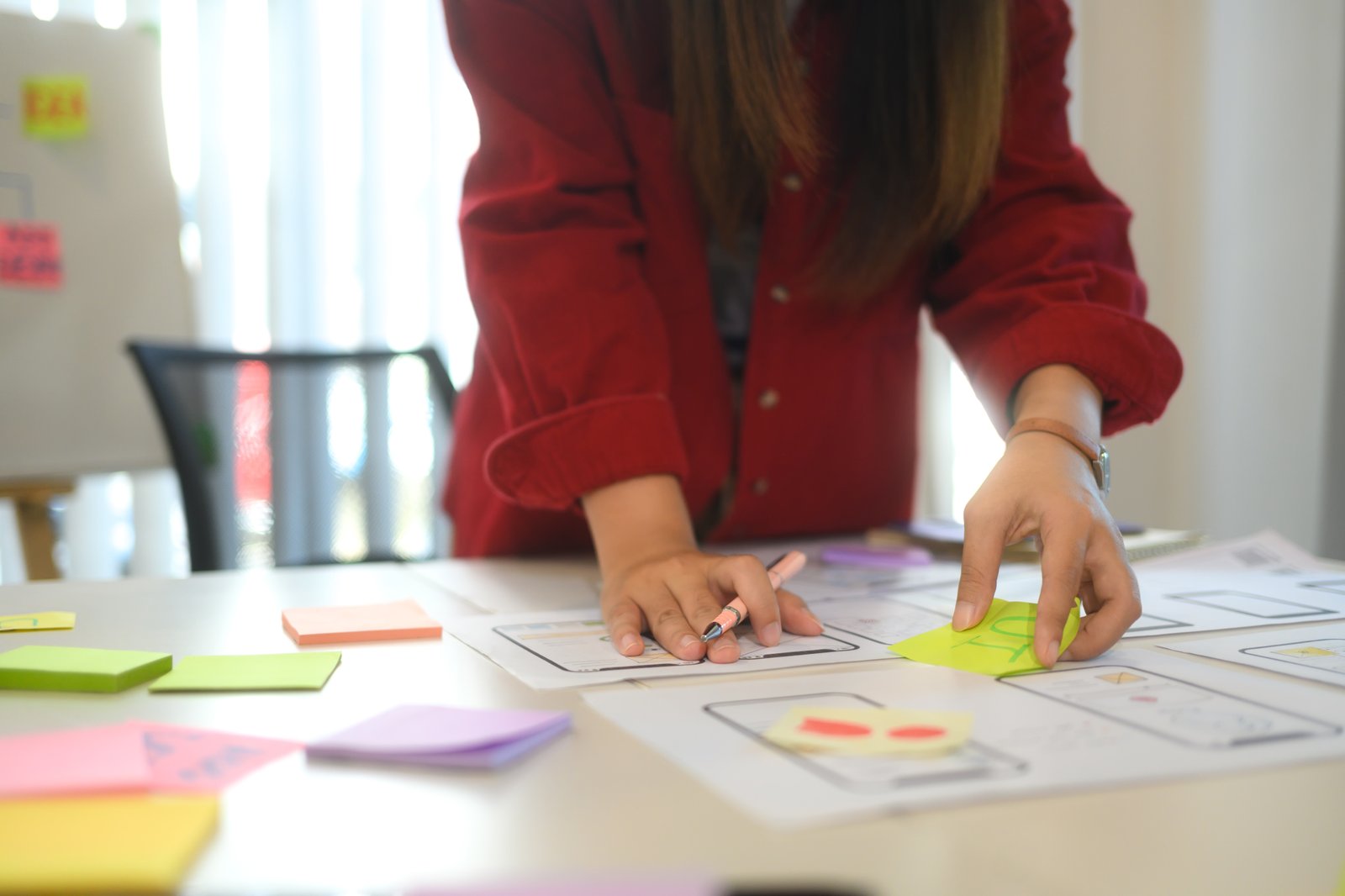 A designer arranging sticky notes and wireframes during a design thinking workshop A designer arranging sticky notes and wireframes during a design thinking workshop