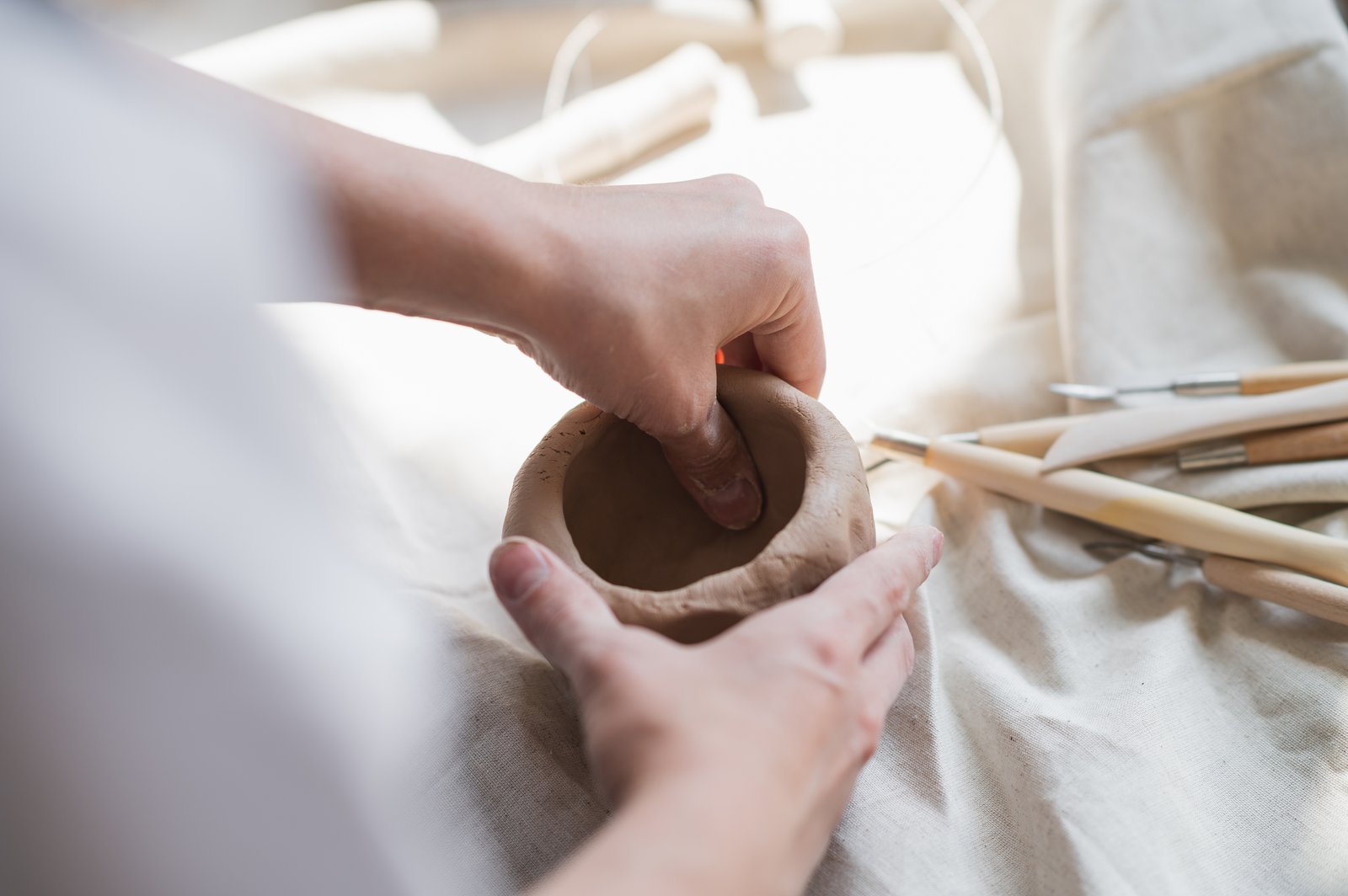 Hands shaping a small clay pot, a clear example of handicraft